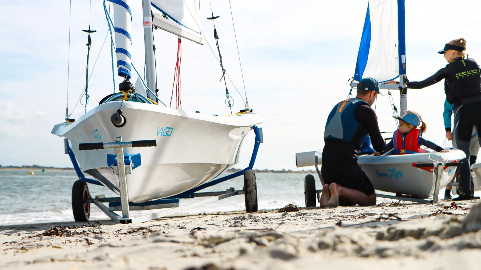 OceanPlay-Jollen Vago und Pico auf Slipwagen am Strand, ein Kind wird in die Pico gesetzt