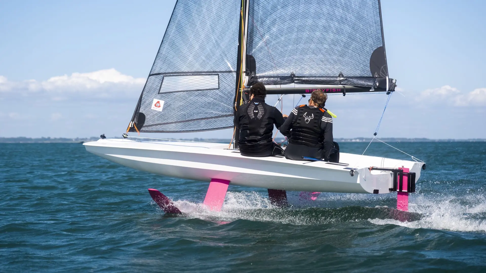 Foiling-Segeljolle BirdyFish mit zwei Personen hebt auf pinken Foils ab